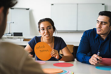 Studentin hält ein Blatt mit der Notiz "Critical Thinking" in die Höhe